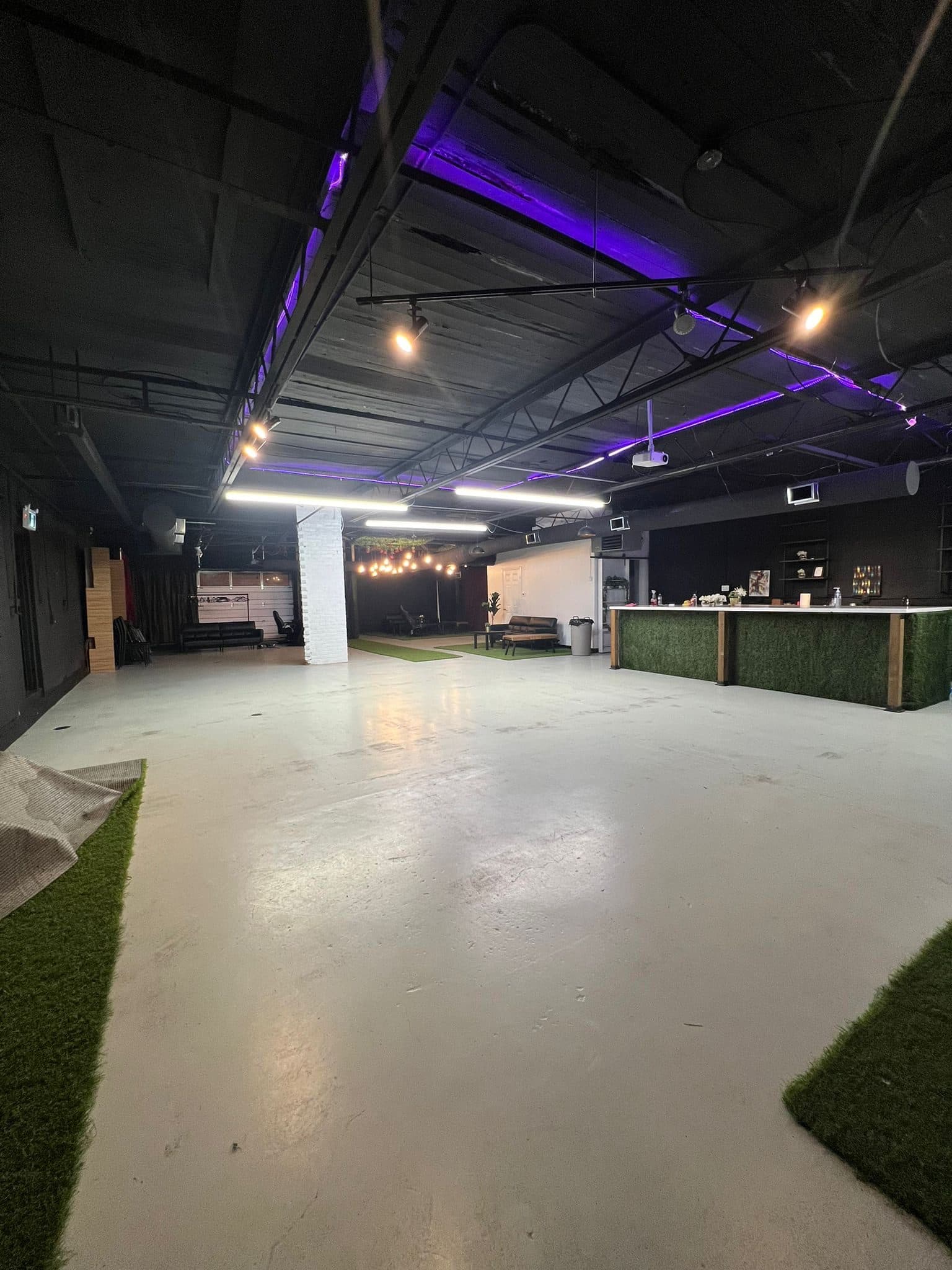 Half Note's cleared event floor under purple LED strip lighting, with a garage door at the back and the turf-fronted presentation bar on the right.