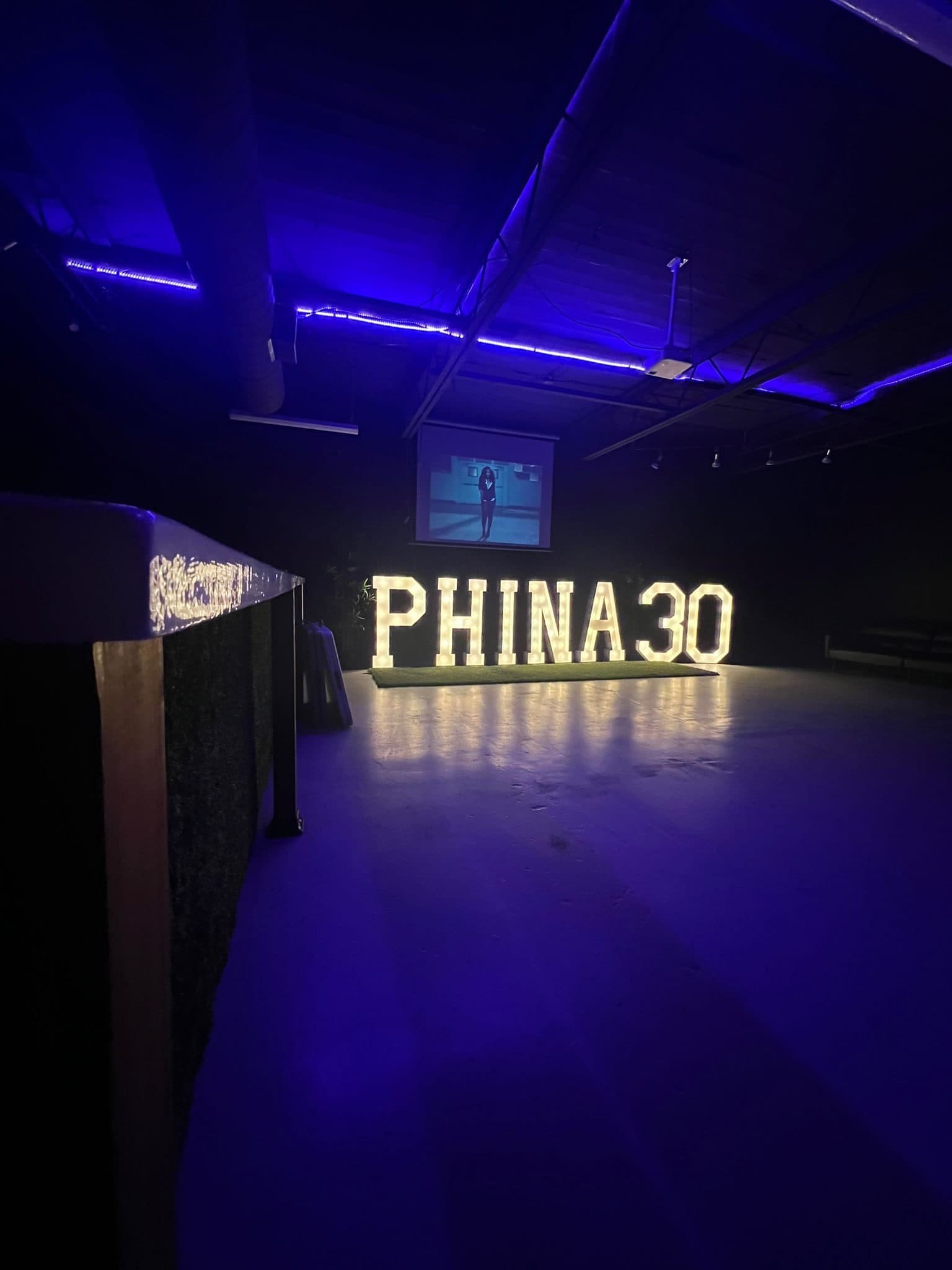 A 30th birthday at Half Note: lit marquee letters spelling PHINA 30 on the floor under purple lighting, with a video on the projector screen.