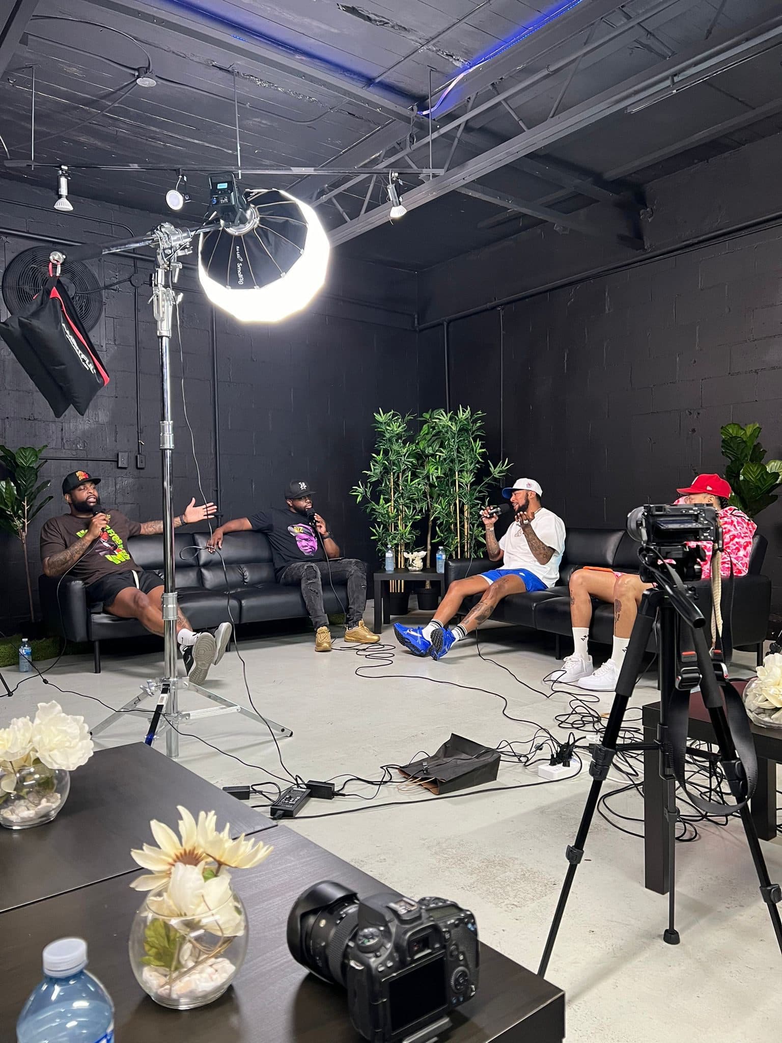 A podcast recording at Half Note: four people on black sofas with microphones, filmed by cameras on tripods under a large studio light.