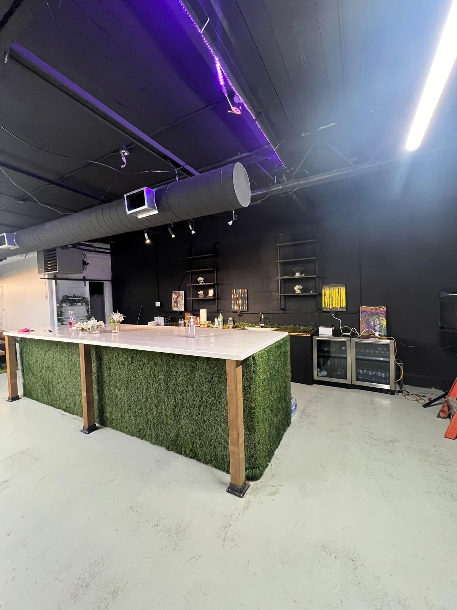 The presentation bar at Half Note: a long white counter with a turf front, with shelving and drinks fridges behind it.