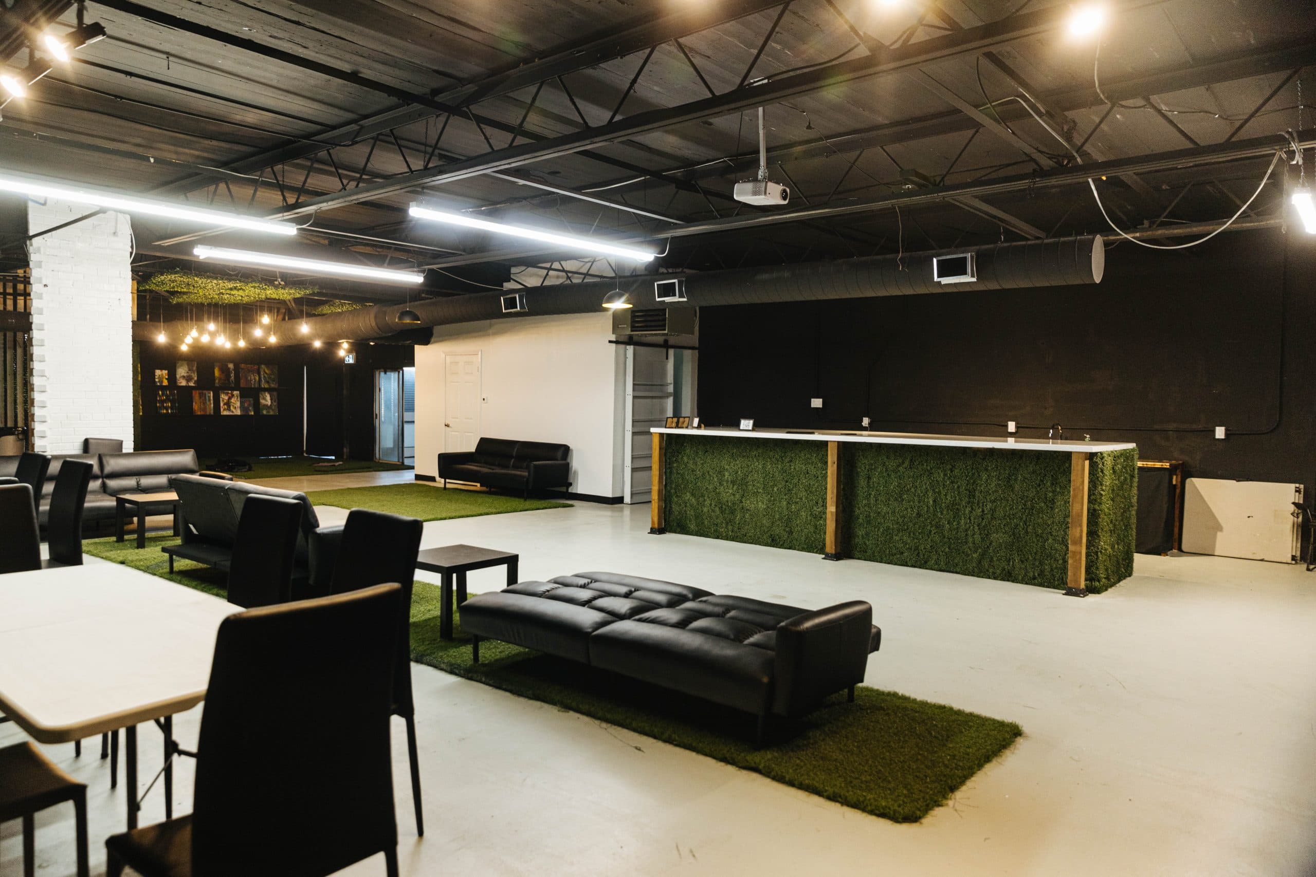 The presentation bar at Half Note, with its turf front and white counter, beside black leather sofas and a ceiling-mounted projector.