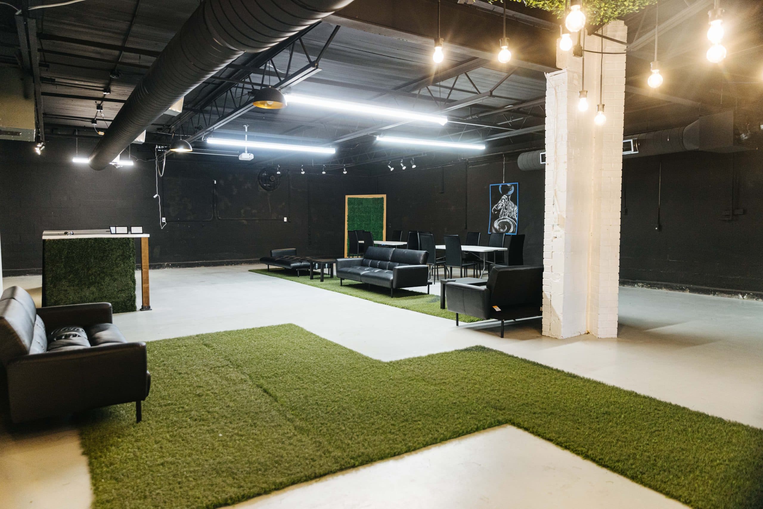Half Note's open floor, with black walls, exposed ceilings, hanging Edison bulbs and black leather lounge seating on turf.